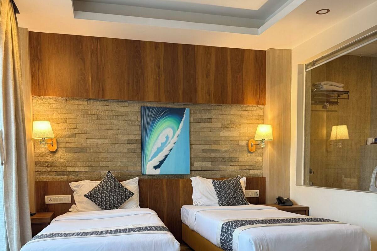 A hotel room with two beds, wooden paneling on the walls, a large abstract painting, and a bathroom visible through a glass door.