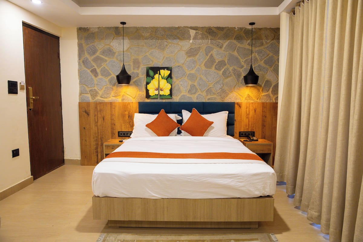 A bedroom with a stone wall, a bed with white bedding and orange pillows, two bedside tables with lamps, and a wooden door.