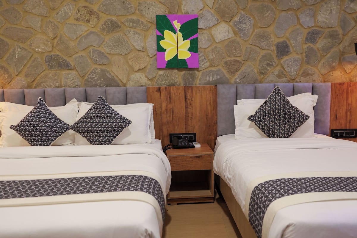 A hotel room with two beds, a stone wall, a wooden headboard, and a painting of a flower.