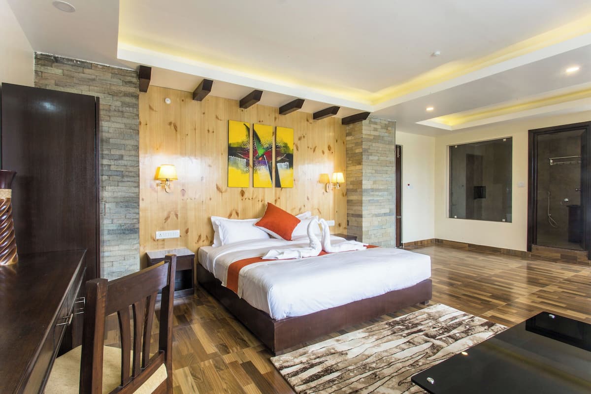 A modern hotel room with a wooden headboard, a large bed with white bedding and orange pillows, two wall-mounted lamps, and a wooden desk with a chair.