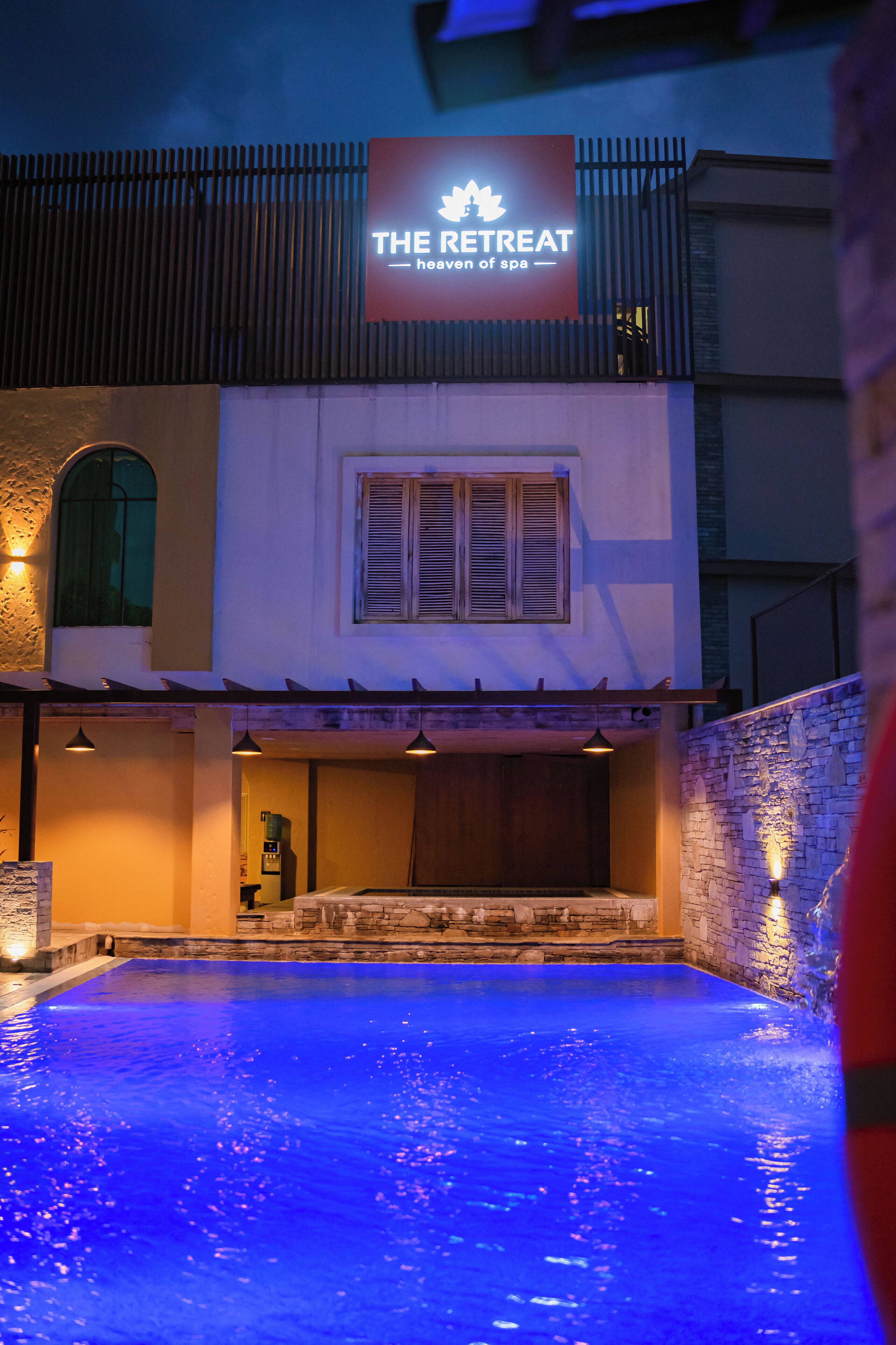 Un bâtiment sur lequel on peut lire l’inscription « The Retreat », ainsi qu’un espace piscine doté de murs en pierre et d’une terrasse en bois.