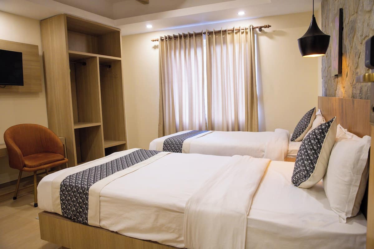 A hotel room with two beds, a wooden wardrobe, a chair, and a television.
