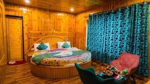 Quarto de madeira com cama redonda, uma cadeira e uma mesa com frutas.