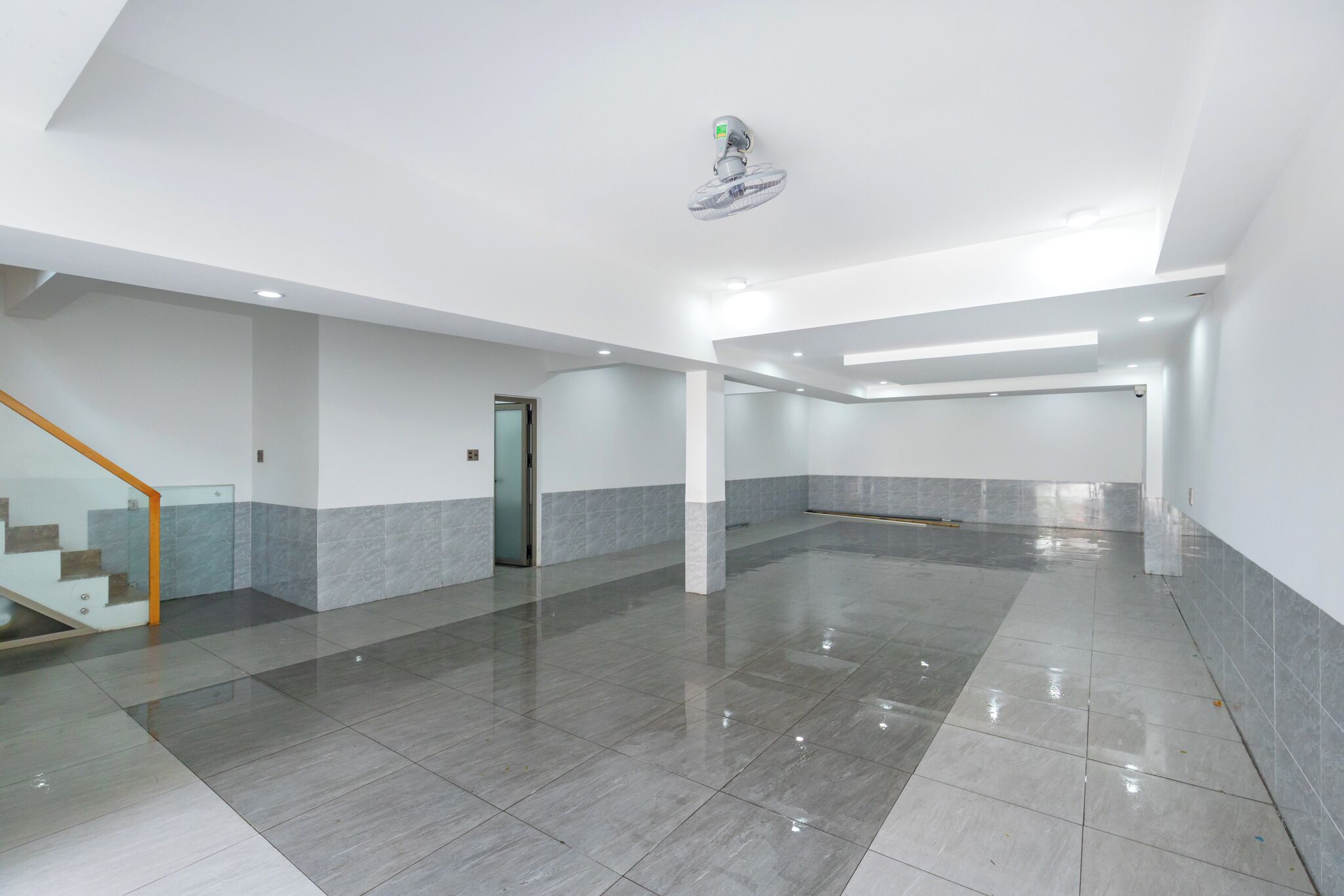 A spacious, modern lobby with a polished tile floor, a glass staircase, and a ceiling fan.