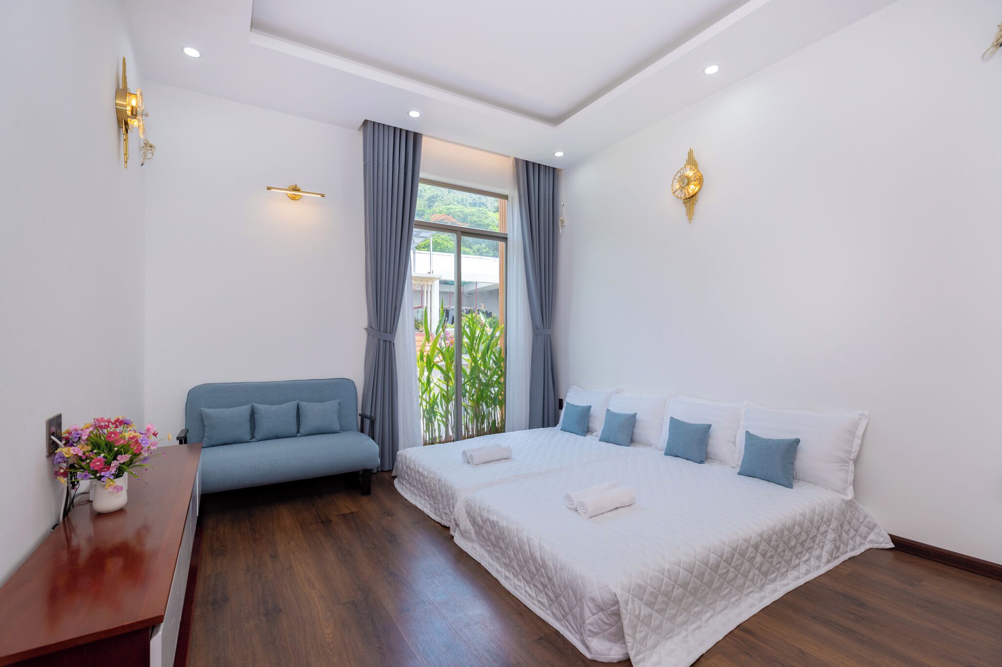 Una habitación de hotel con cama, sofá, escritorio de madera y ventana con cortinas.