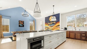 Eine moderne Küche mit einer großen Kochinsel, weißen Schränken und einer Spritzschutzwand mit einem Wandgemälde mit dem Schriftzug 'Stay Groovy Austin'.