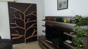 A modern living room with a dark wooden TV stand, a black wall-mounted TV, and a decorative tree-like panel. - Luxury Apartment with Mountain View and Parking in Tetouan (Tétouan)