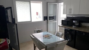 A compact kitchen with a dining table, chairs, a washing machine, and a microwave. - Luxury Apartment with Mountain View and Parking in Tetouan (Tétouan)