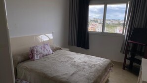 A bedroom with a bed, a window with curtains, and a view of buildings outside. - Luxury Apartment with Mountain View and Parking in Tetouan (Tétouan)