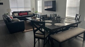 Ein modernes Wohnzimmer mit einem dunkelgrauen Ledersofa, einem Couchtisch und einem Esstisch mit Stühlen.