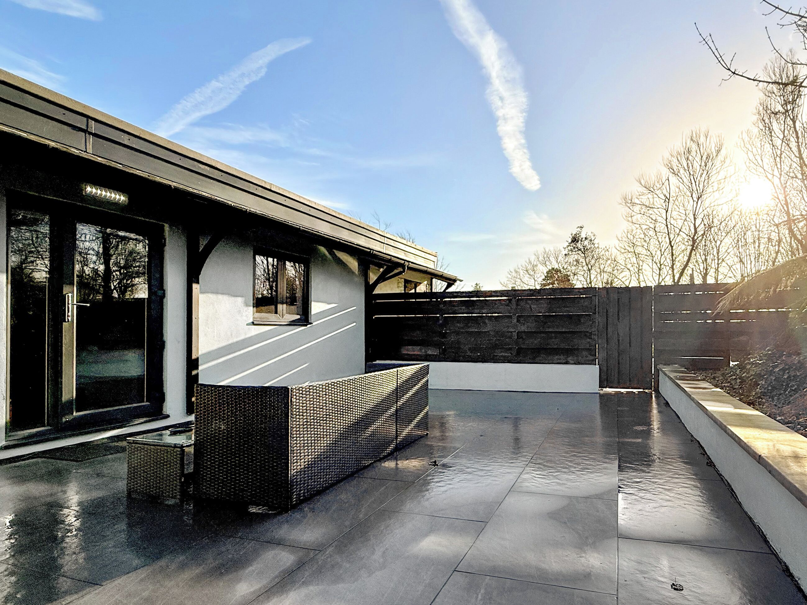 Un bâtiment moderne doté d’une façade en verre, d’un espace extérieur couvert et d’une terrasse dallée.