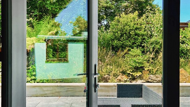 A modern outdoor patio area with a glass door leading to a green wall and lush vegetation.