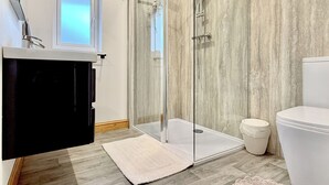 A modern bathroom with a glass shower enclosure, a white toilet, and a wooden floor.