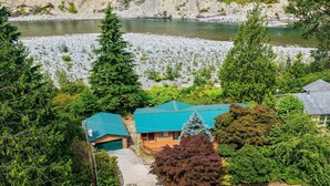 A lodge with a stone foundation, a wooden deck, and a view of a river. - Prospector's Bend - Hot Tub, Riverfront, Fishing (Gold Bar)