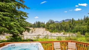 A hot tub on a wooden deck with chairs, overlooking a river and forested mountains. - Prospector's Bend - Hot Tub, Riverfront, Fishing (Gold Bar)