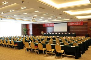 A conference room with rows of tables and chairs, a projection screen, and a banner on the wall. - Blue Horizon International Hotel (Weifang)