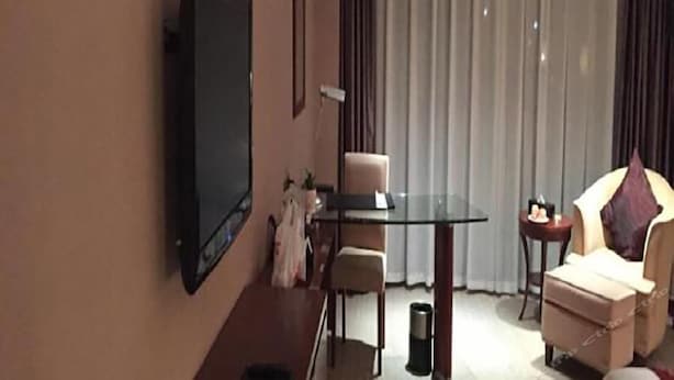 Et hotelværelse med et fladskærms-tv monteret på væggen, et spisebord med glasplade, en sofa og et lille sofabord.