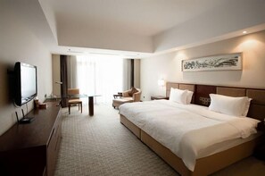 Ein Hotelzimmer mit einem großen Bett, einem Schreibtisch mit Fernseher, einem Sessel und einem Gemälde an der Wand.