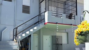 Edifici de dos pisos amb un balcó, una escala i una petita zona exterior amb gespa artificial.