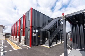 A building with shipping containers, a staircase, and a chain-link fence. - HOTEL R9 The Yard Ushiku (Ushiku)