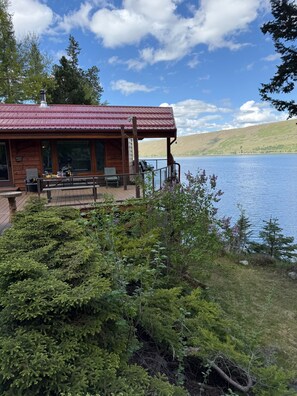 A cabin with a red roof overlooking a lake, a deck with seating, and a 'Welcome to Lake' sign. - Eagle Point Lakeview (Joseph)