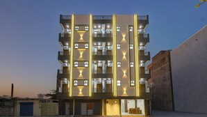 Un edificio de varios pisos con balcones y unidades de aire acondicionado, que presenta un diseño moderno con líneas verticales iluminadas.