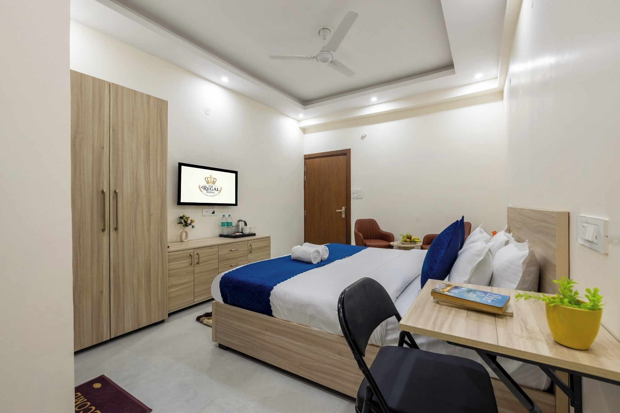 A modern hotel room with a bed, a desk, a chair, a wardrobe, and a ceiling fan.