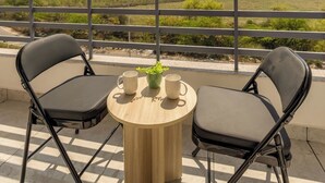 Un balcón con dos sillas, una mesita redonda y vistas a un paisaje urbano lejano.