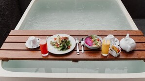 Una mesa de madera con una preparación para el desayuno que incluye un plato de comida, un vaso de jugo de uva, un tazón de ensalada, un vaso de jugo de naranja y un cebrero.