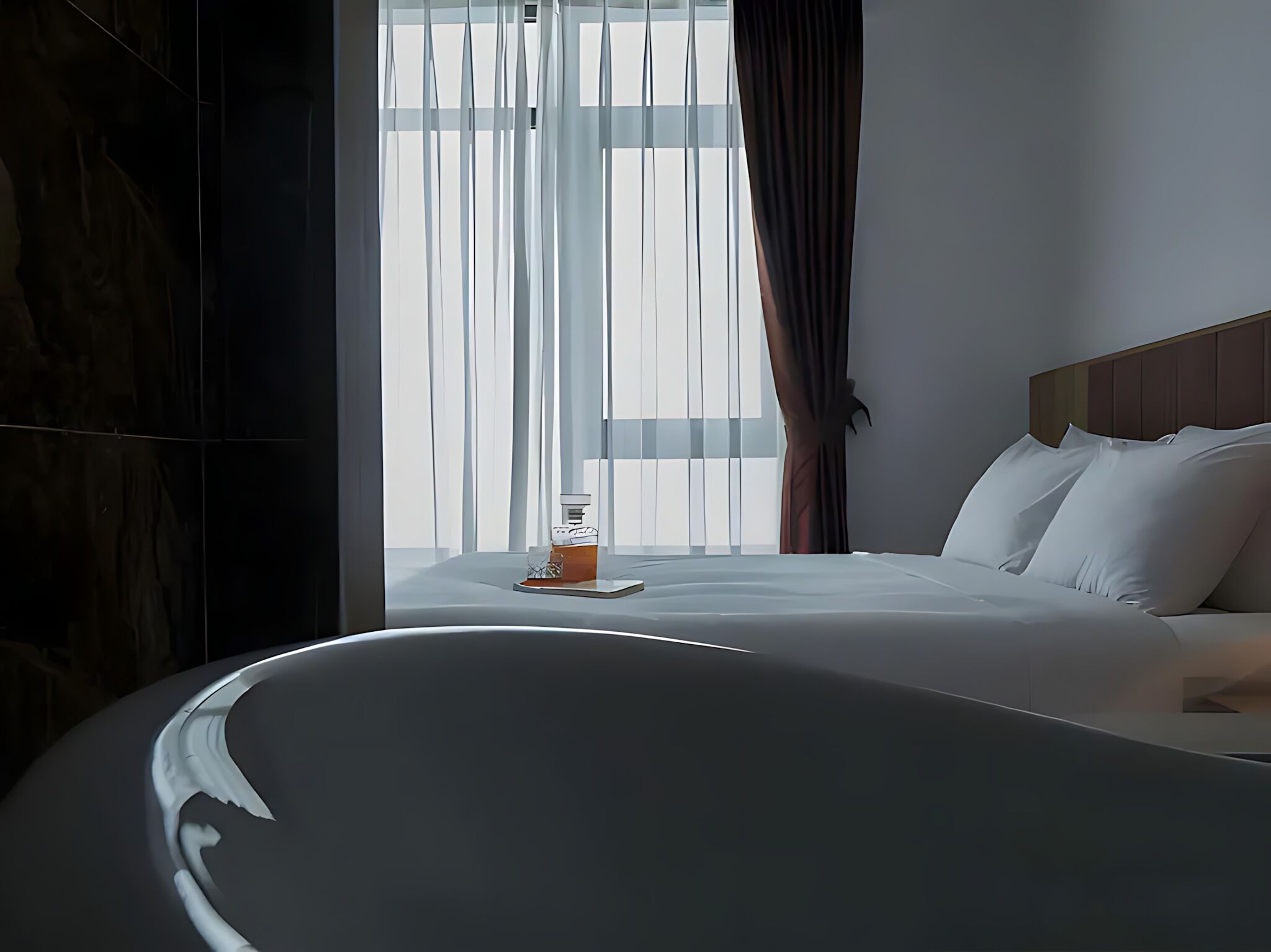 Une chambre d’hôtel moderne avec un grand lit, une baignoire et une vue sur la ville à travers de fines rideaux.