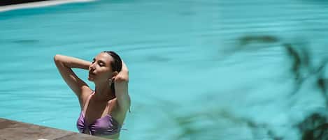 A person in a purple swimsuit by a pool with clear water.
