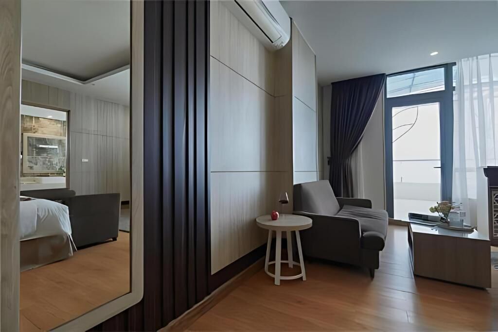 Une chambre d’hôtel moderne, équipée d’un lit, d’une petite table ronde avec une lampe, d’un canapé et d’une grande fenêtre avec des rideaux.