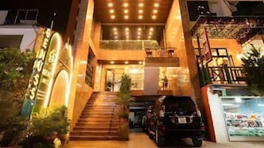 A multi-story hotel with a prominent entrance, a staircase leading to the lobby, and a parking area in front.