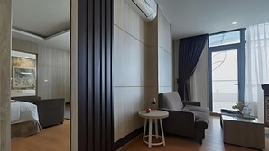 A modern hotel room with a bed, a grey armchair, a small round table, and a large mirror.
