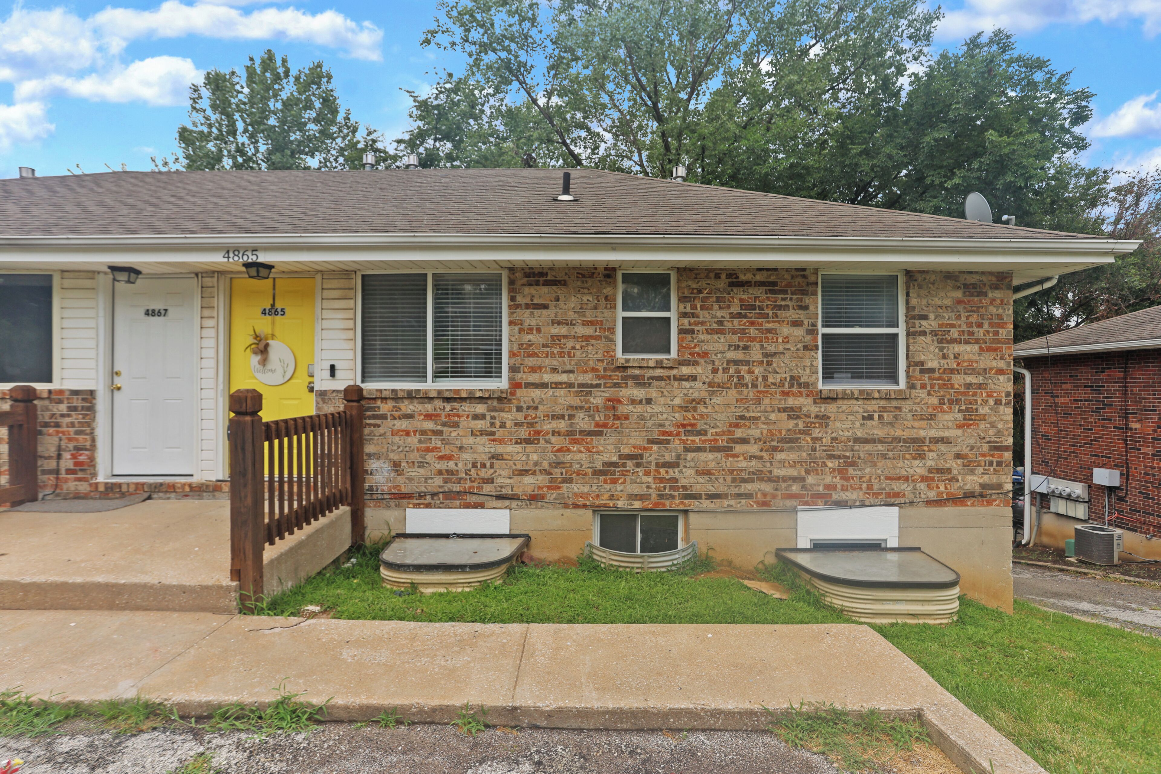 A two-story house with a brick facade, a yellow door, and a small front yard.