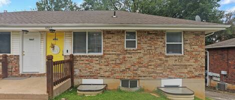 A two-story house with a brick facade, a yellow door, and a small front yard.