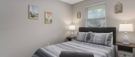 A bedroom with a large bed, two bedside tables with lamps, a ceiling fan, and two framed pictures on the wall.