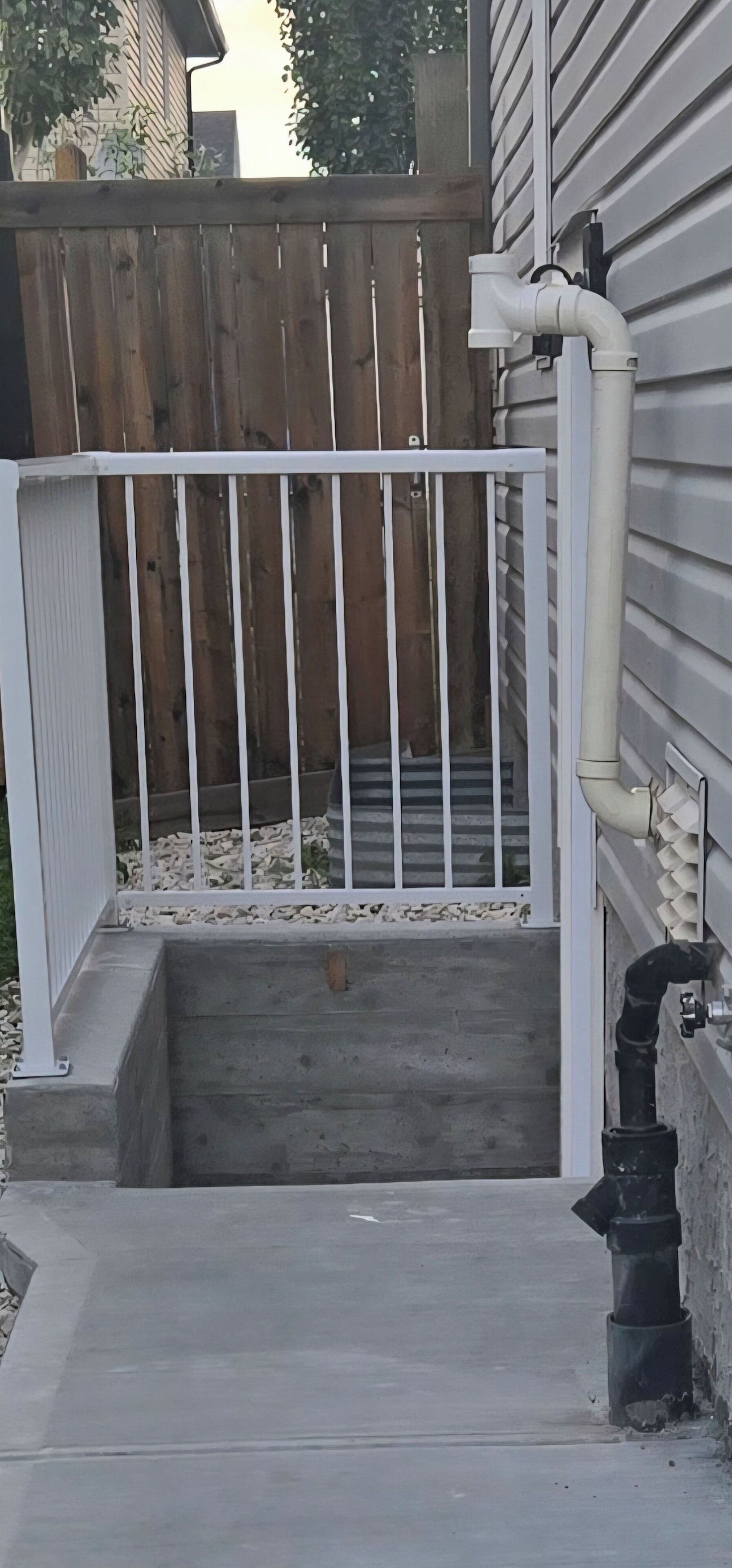 Un tramo de escalones de hormigón que conduce a una zona vallada con cerca de madera y barandilla blanca.