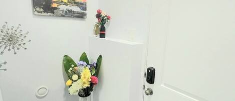 Un couloir avec une porte blanche, un tableau accroché au mur et un vase rempli de fleurs.