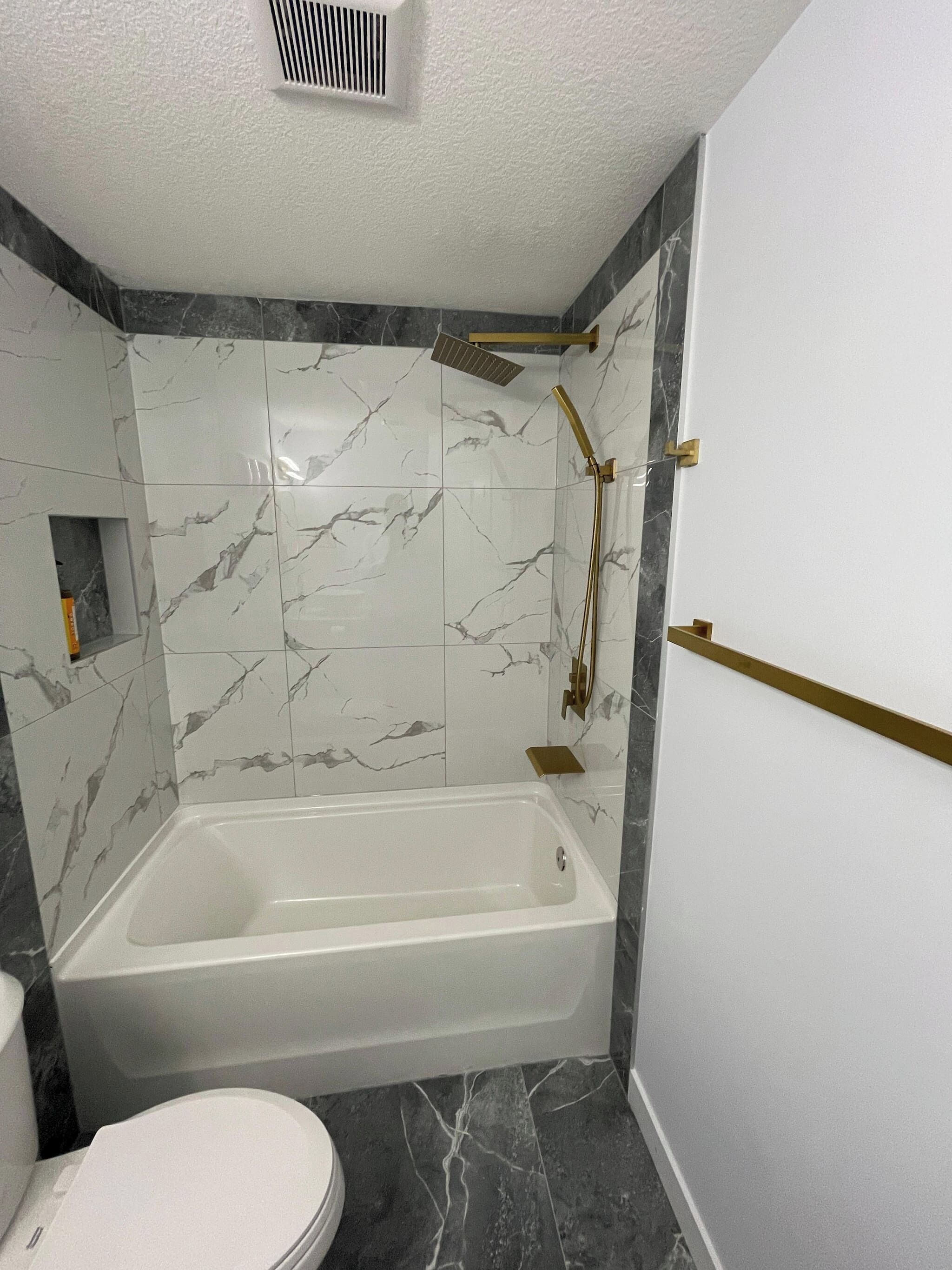 Ein Badezimmer mit einer Badewanne, einer Toilette und einem Duschbereich mit Marmorfliesen.