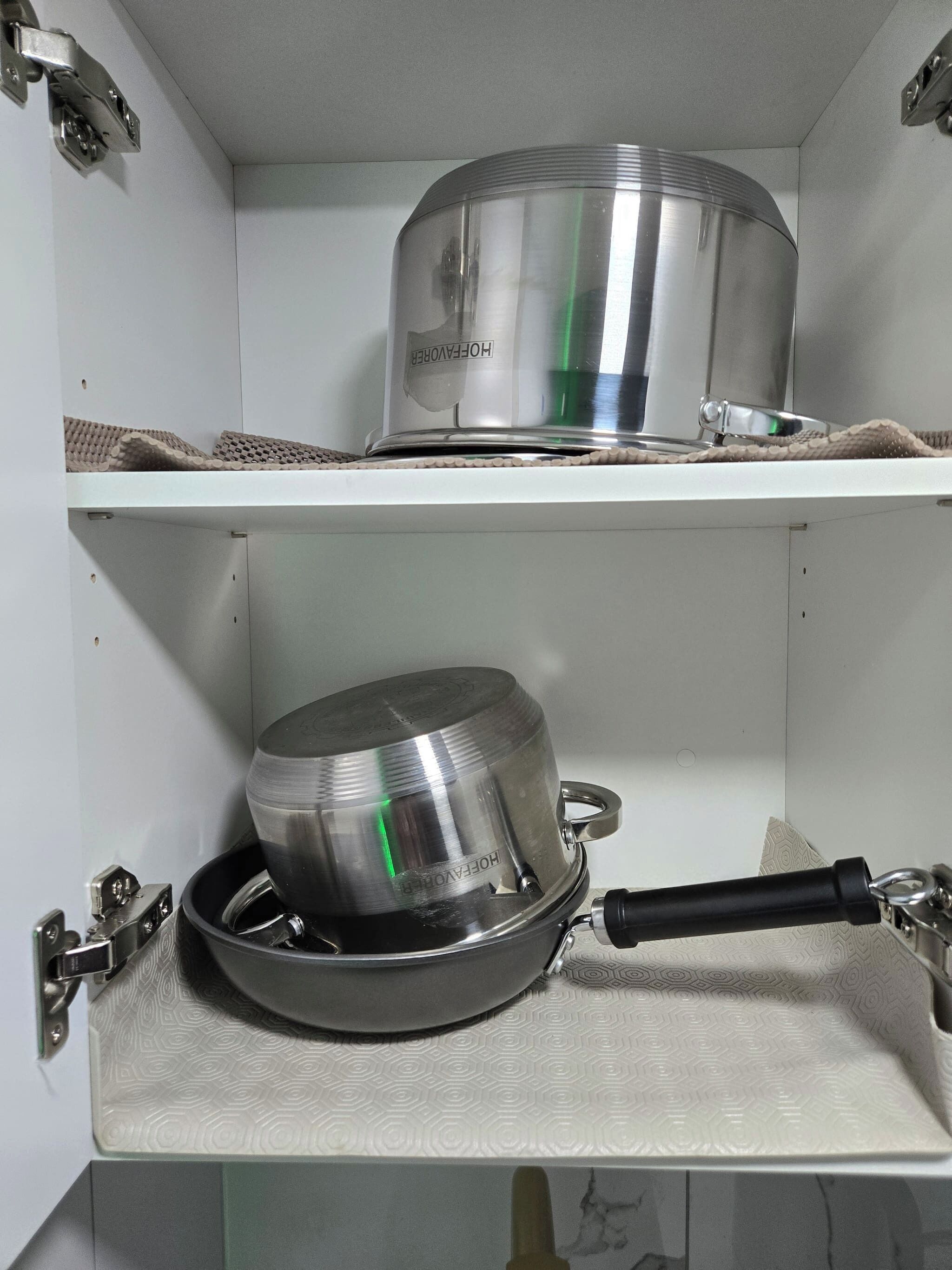 Une cuisine avec deux casseroles en acier inoxydable posées sur des étagères.