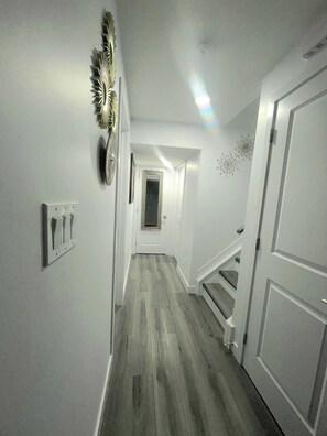 A narrow hallway with a wooden floor, white walls, and a staircase leading to another level. - A Place of Refuge and Comfort (Edmonton)