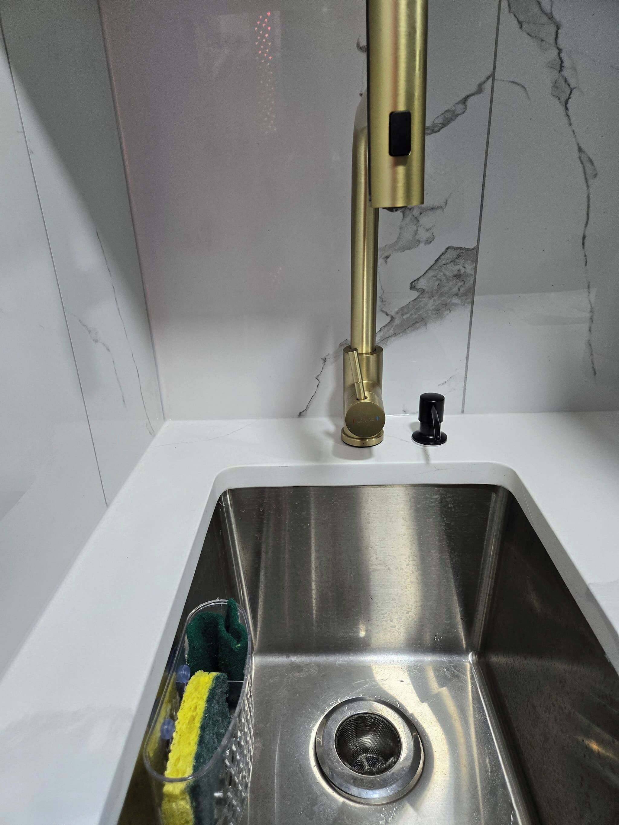 Una lavandino in acciaio inox con un rubinetto dorato, uno scarico e una spugna verde e gialla.