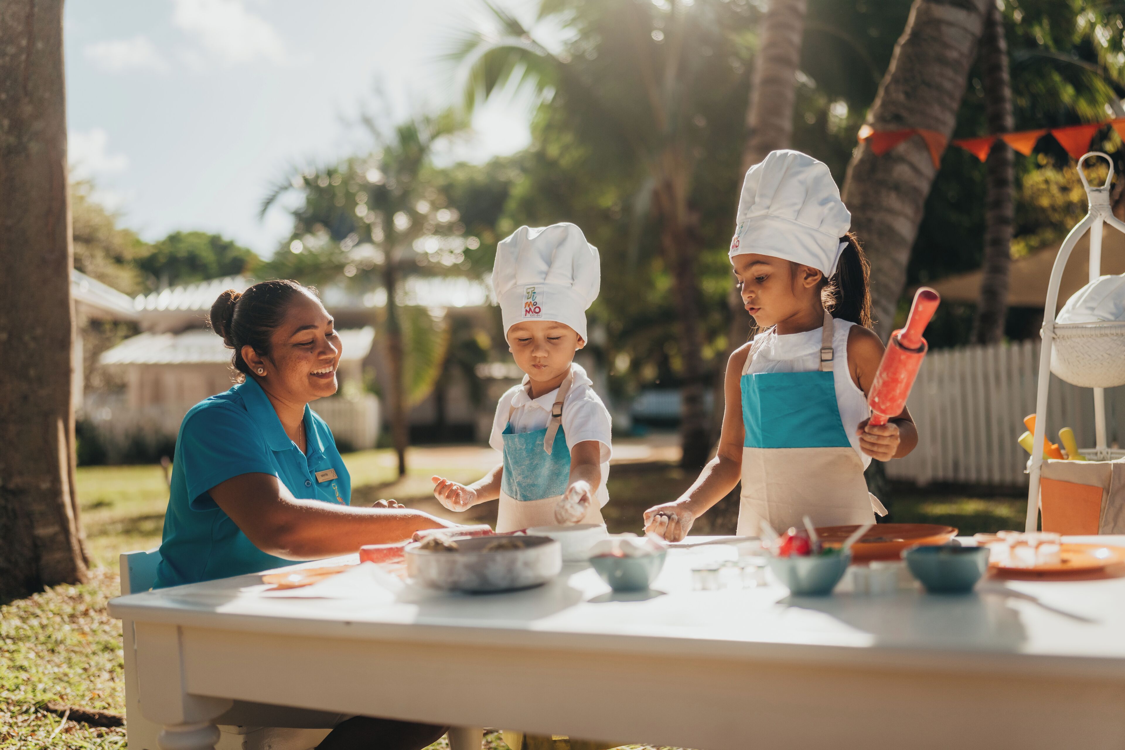 A table with food items and utensils, a person in a chef's hat, and a person in a blue shirt.