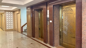 A hallway with a polished stone floor, a wooden panel with triangular cutouts, and a set of elevators with glass doors. - Palette Luxe Jomtien Beach Pattaya (Pattaya)