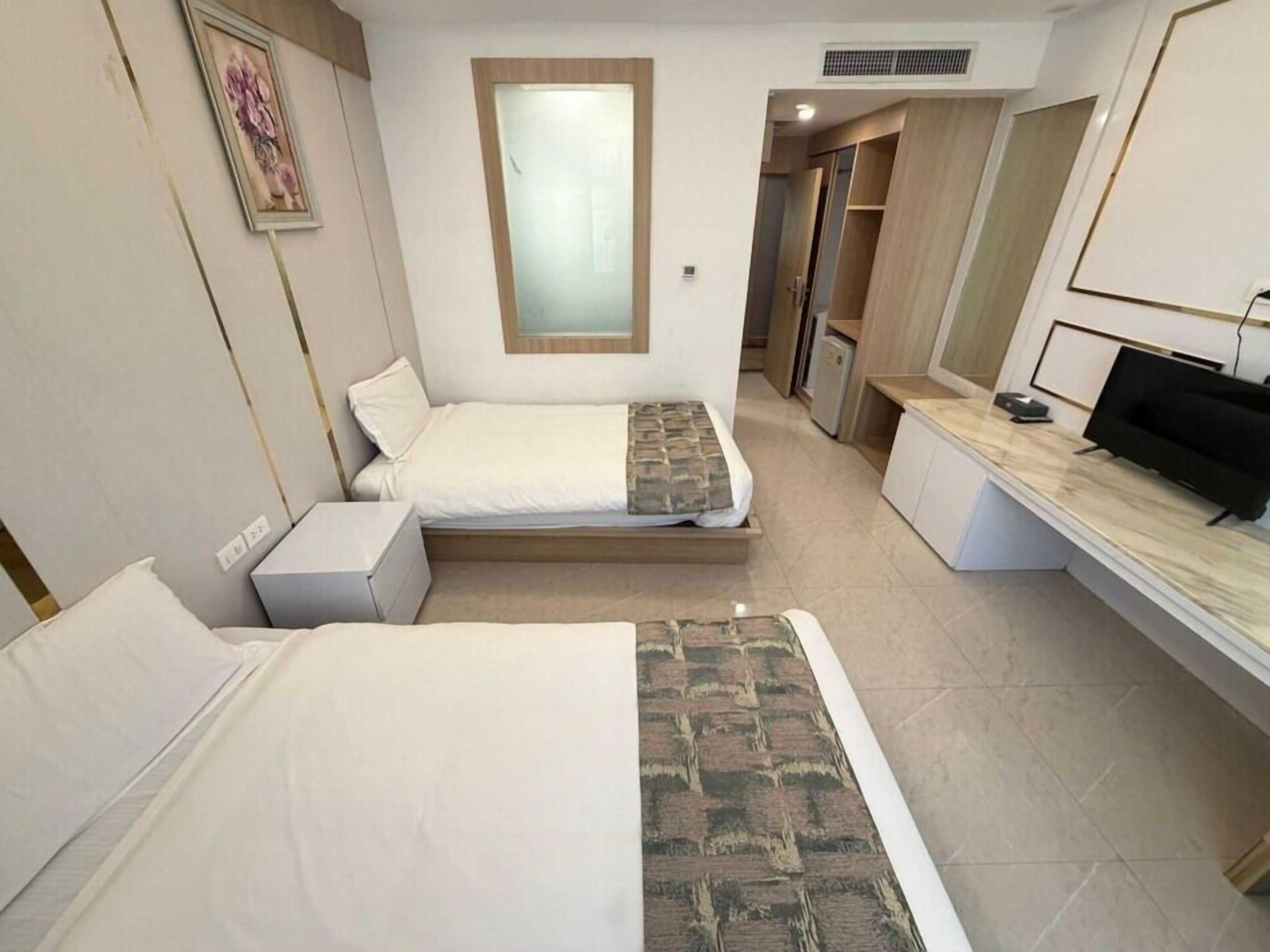 A hotel room with two beds, a desk, a TV, and a bathroom visible through an open door.