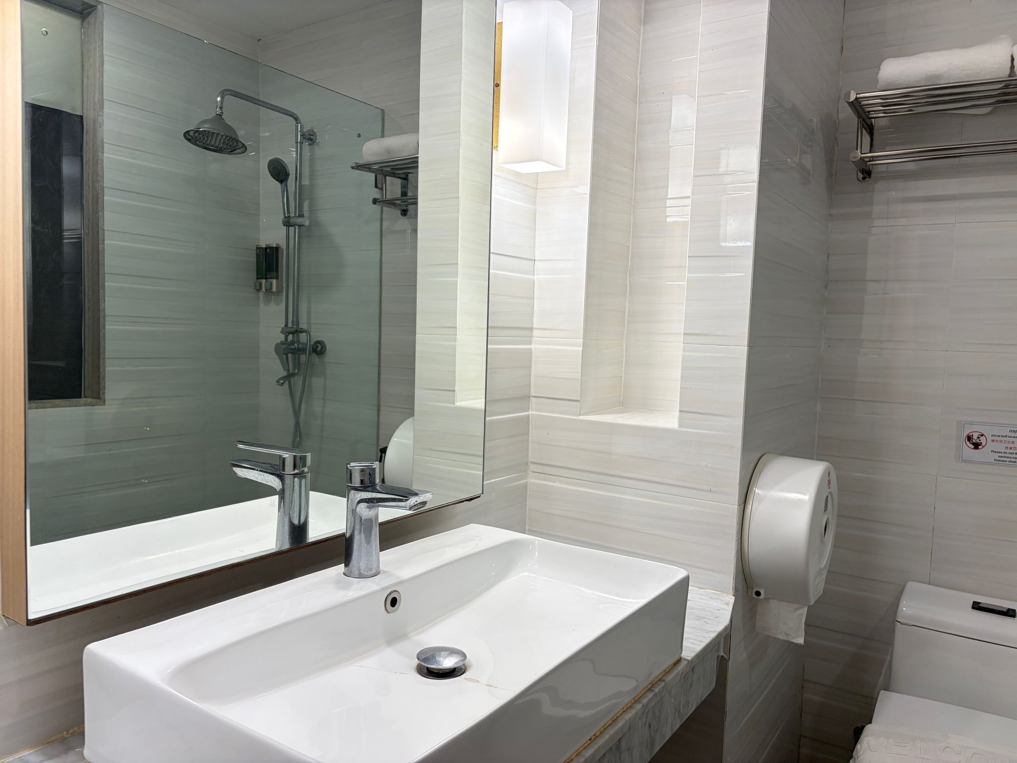 Uma casa de banho moderna com lavatório branco, cabine de duche em vidro e sanita com dispensador de papel.