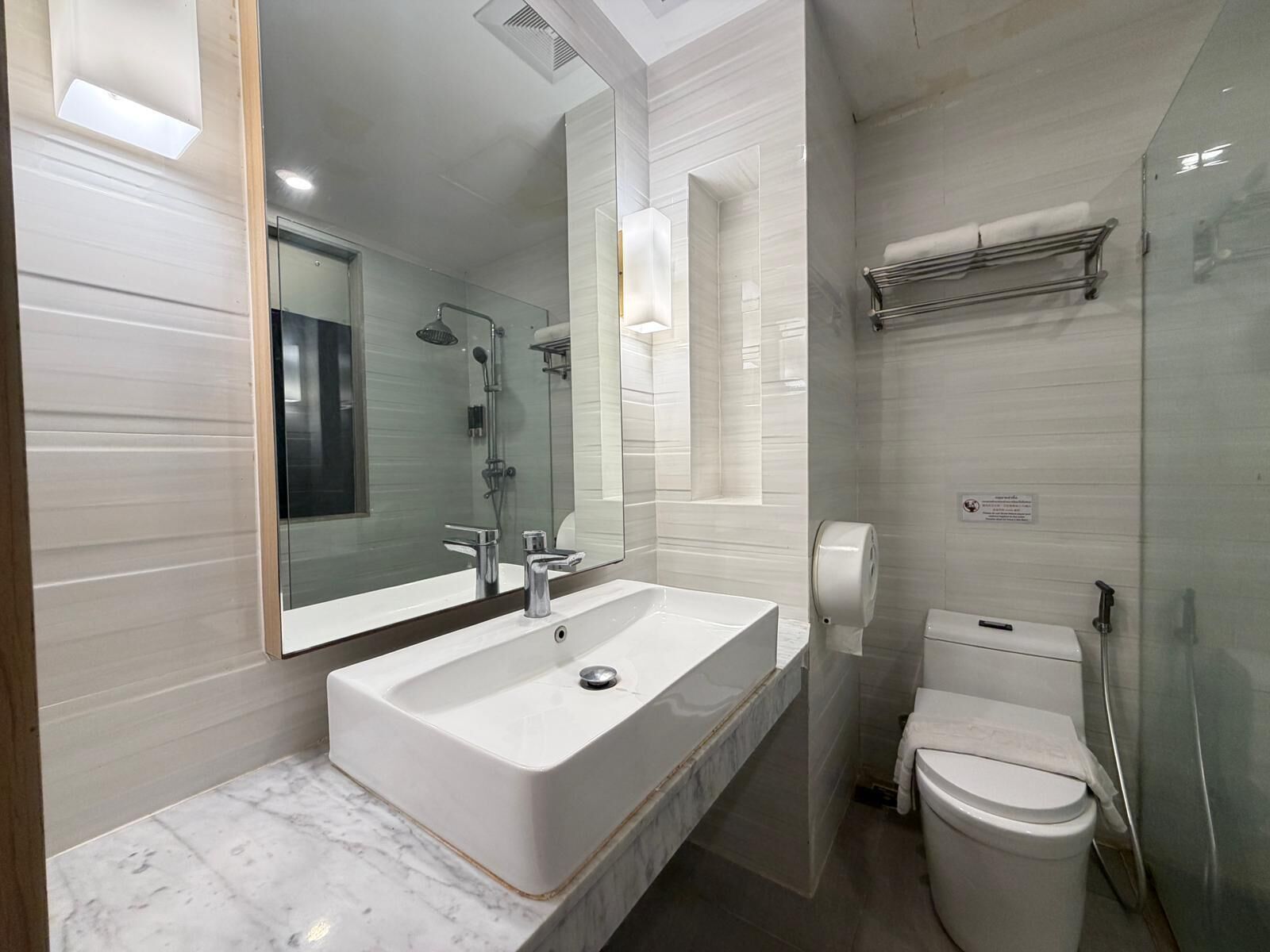 A modern bathroom with a large white sink, a mirror, a shower, and a toilet.