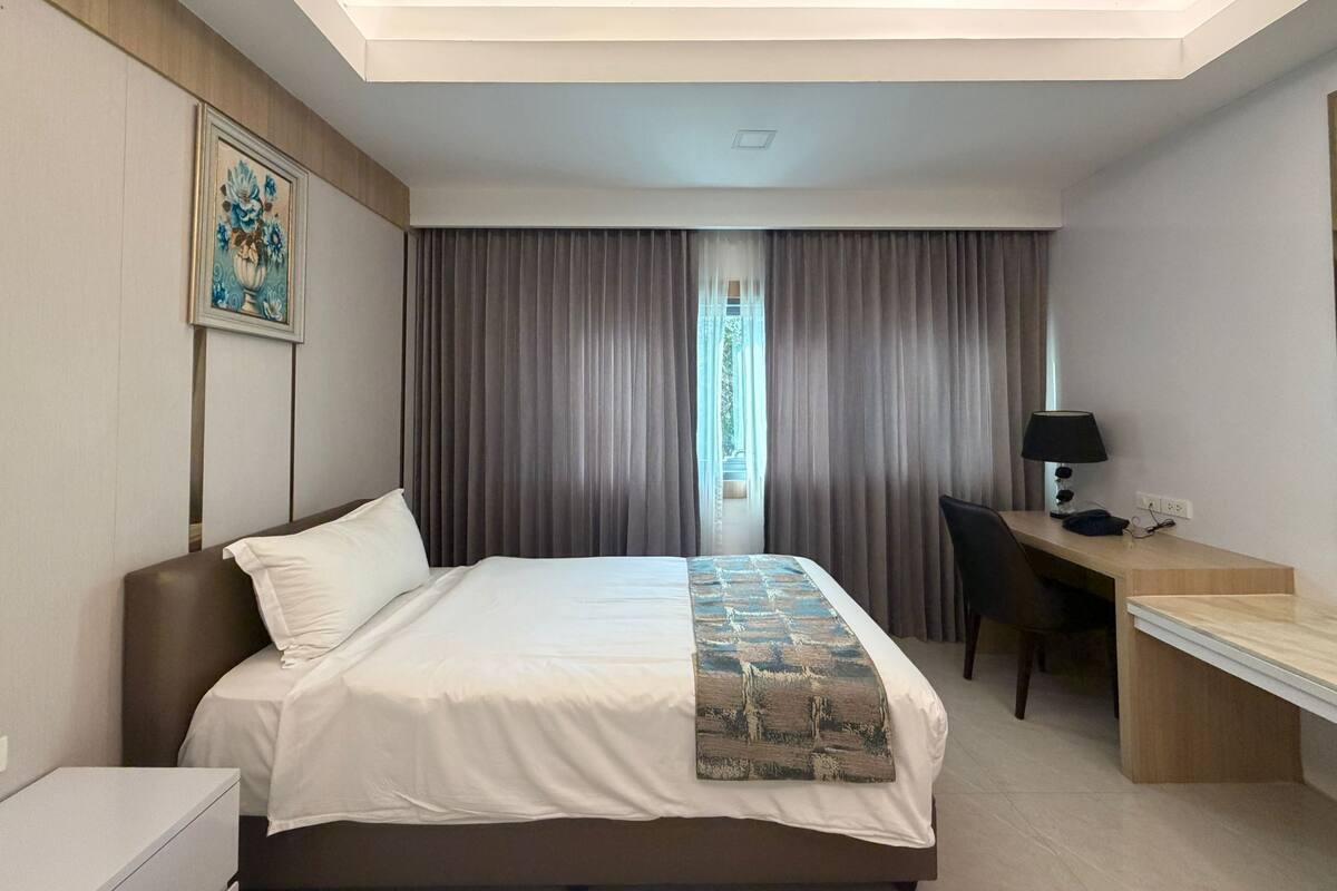 Una habitación de hotel con cama, escritorio, silla, lámpara y un cuadro en la pared.