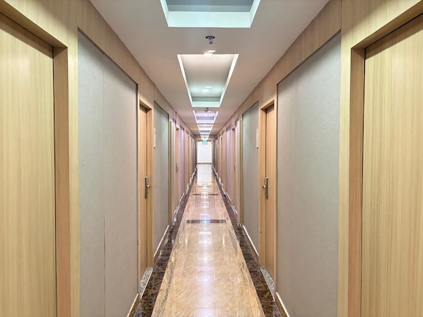 Un long couloir étroit, bordé de portes en bois de part et d’autre, qui mène à un espace lumineux et bien éclairé.